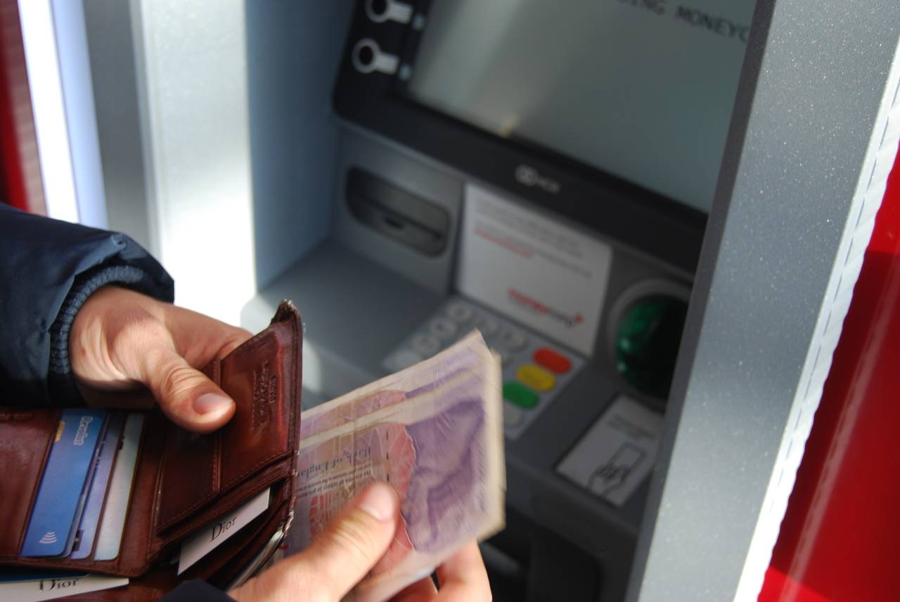 Mężczyzna wypłaca pieniądze z bankomatu