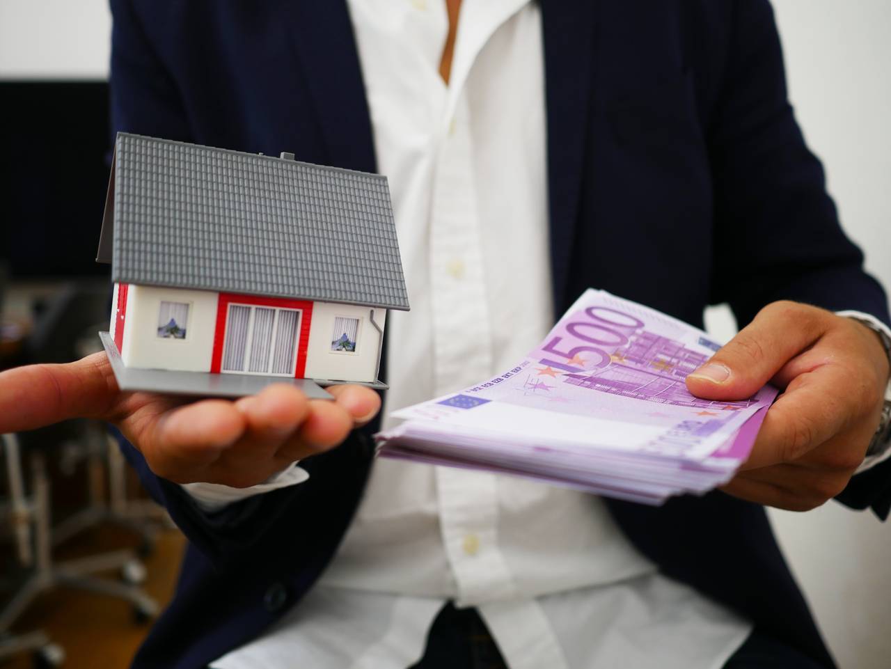 Mężczyzna trzyma w dłoniach pieniądze oraz dom jako symbol dobrej historii kredytowej