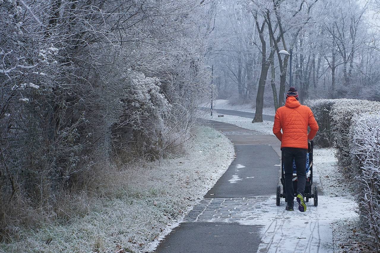 Tata ubrany w zimową kurtkę prowadzi wózek z dzieckiem na spacerze